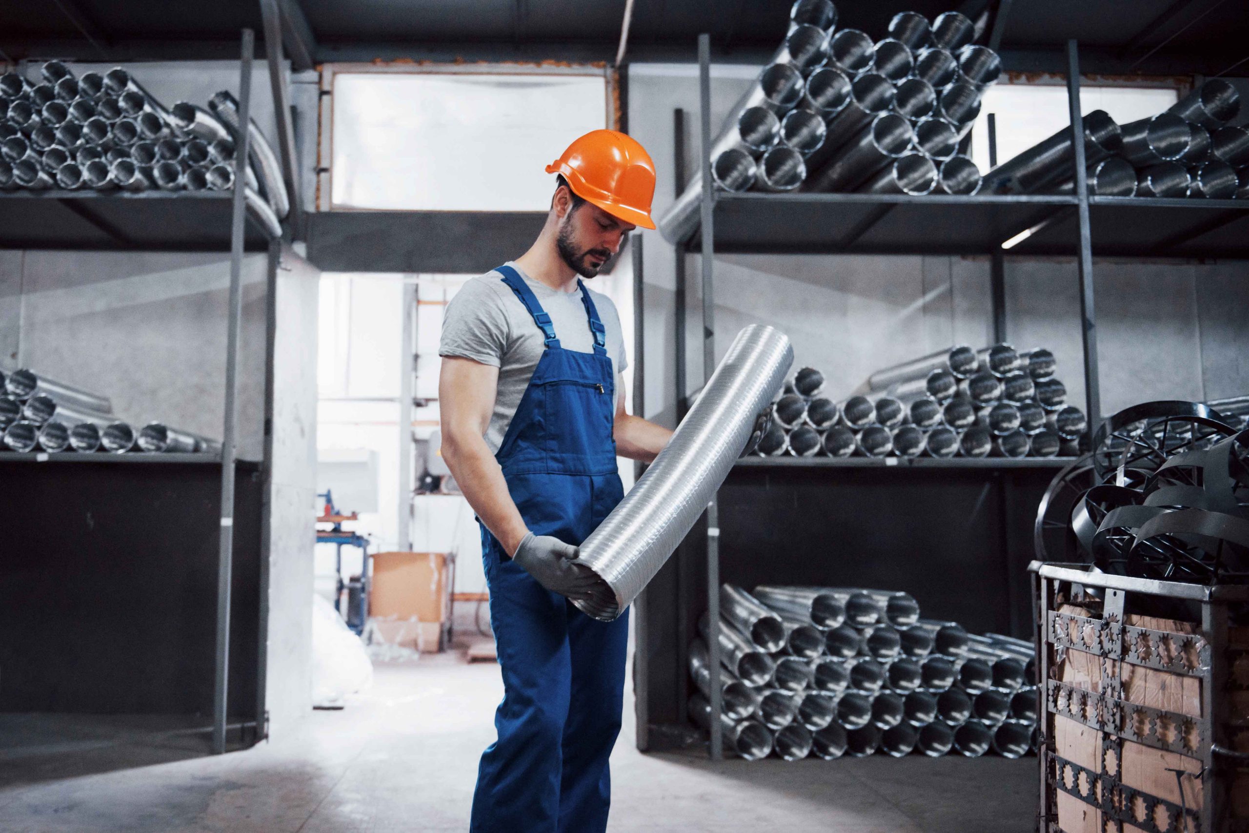 Portrait of a young worker in a hard hat at a large metalworking plant. Shiftman on the warehouse of finished products.